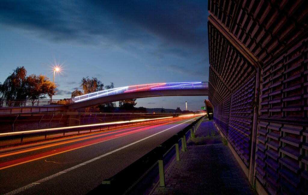 Moderní RGB LED designové osvětlení zasazené přímo do umělecky pojatého zábradlí na lávce pro pěší přes dálnici D5.